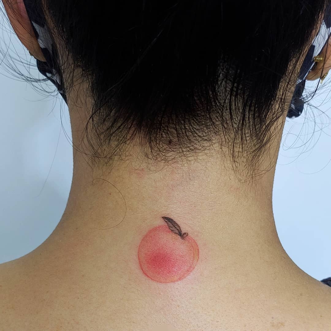Tattoo of a small peach with a leaf on the back of the neck